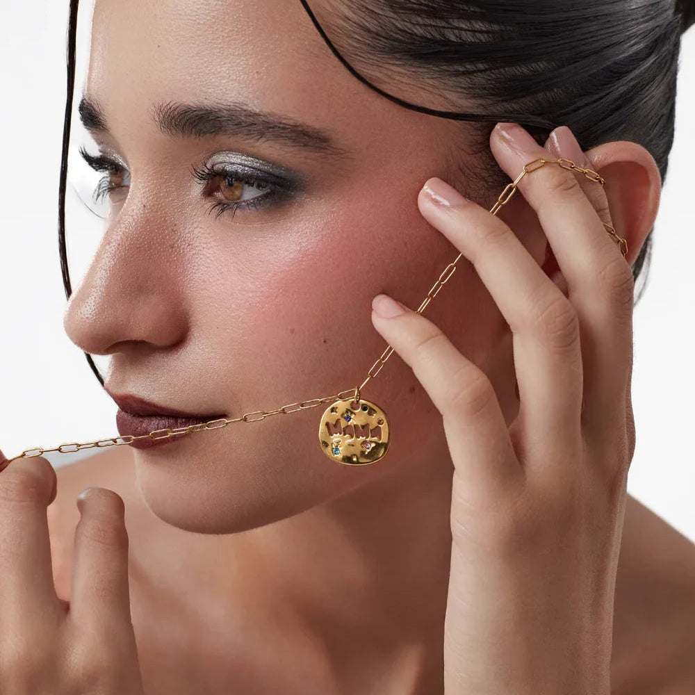 Woman adjusting a gold necklace with a pendant on a neutral background
