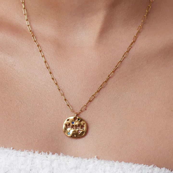 Gold necklace with a circular pendant on a person wearing a white garment.