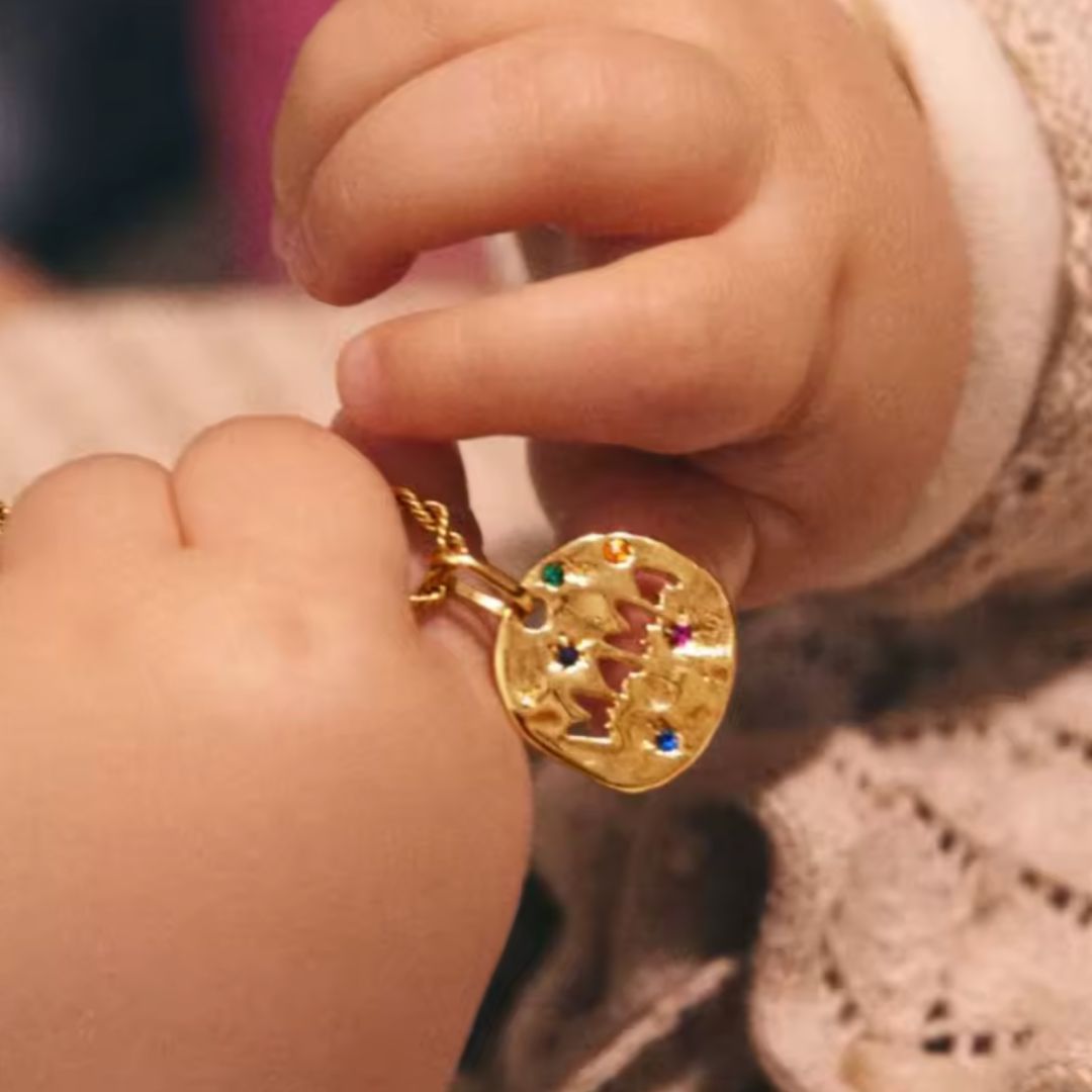 Gold necklace with a colorful pendant held by a child's hand.