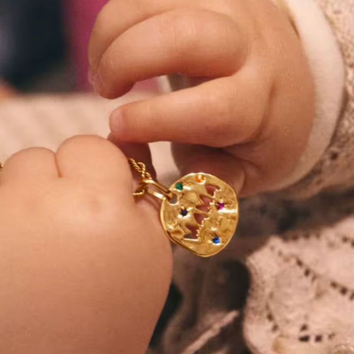Gold necklace with a colorful pendant held by a child's hand.