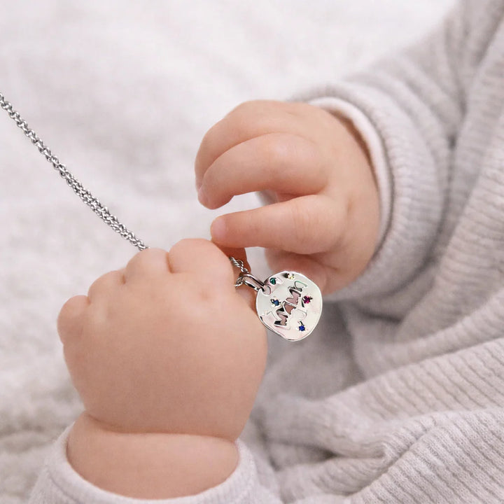 Child's hand holding a necklace with a colorful pendant against a neutral background