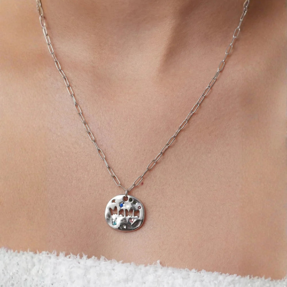 Silver necklace with a round pendant on a person wearing a white top.