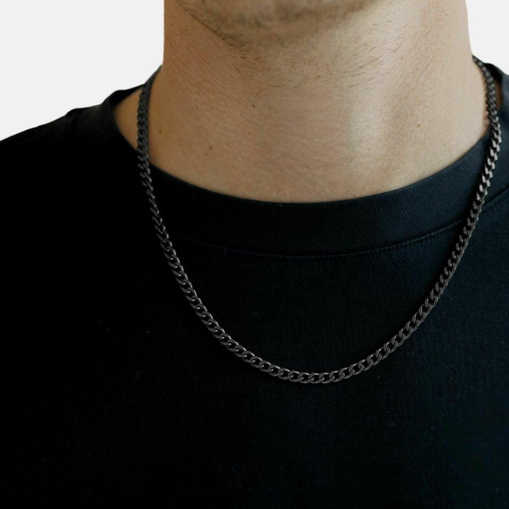 Person wearing a black chain necklace on a plain background