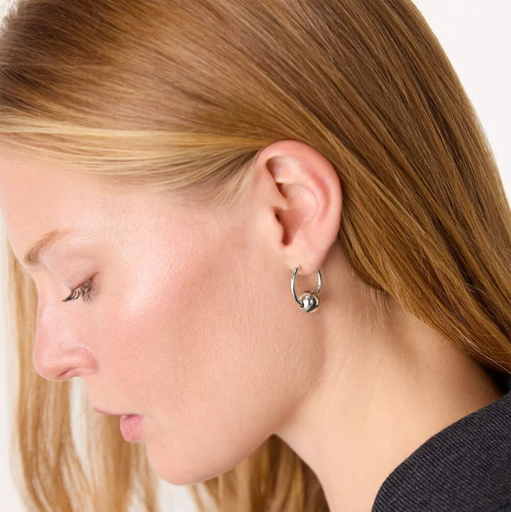 Close-up of a person wearing a silver hoop earring on a white background