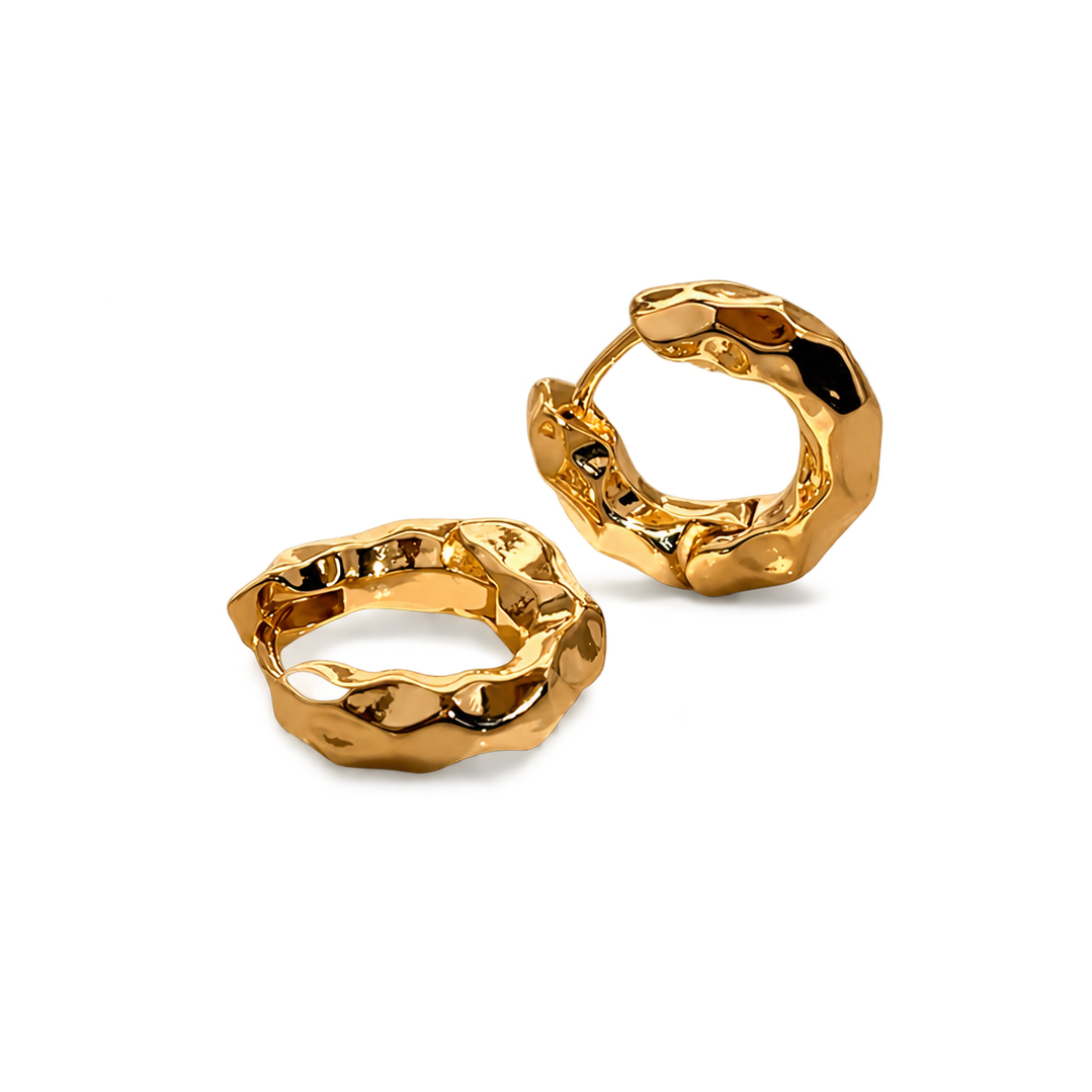 A pair of chunky, textured gold huggie hoop earrings with a polished, organic, hammered finish, displayed on a clean white background.
