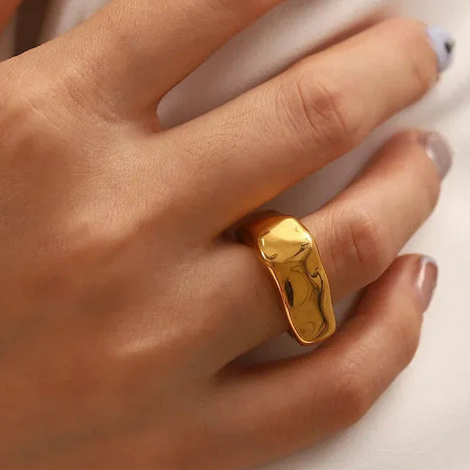 Gold chunky ring on a person's finger against a white background