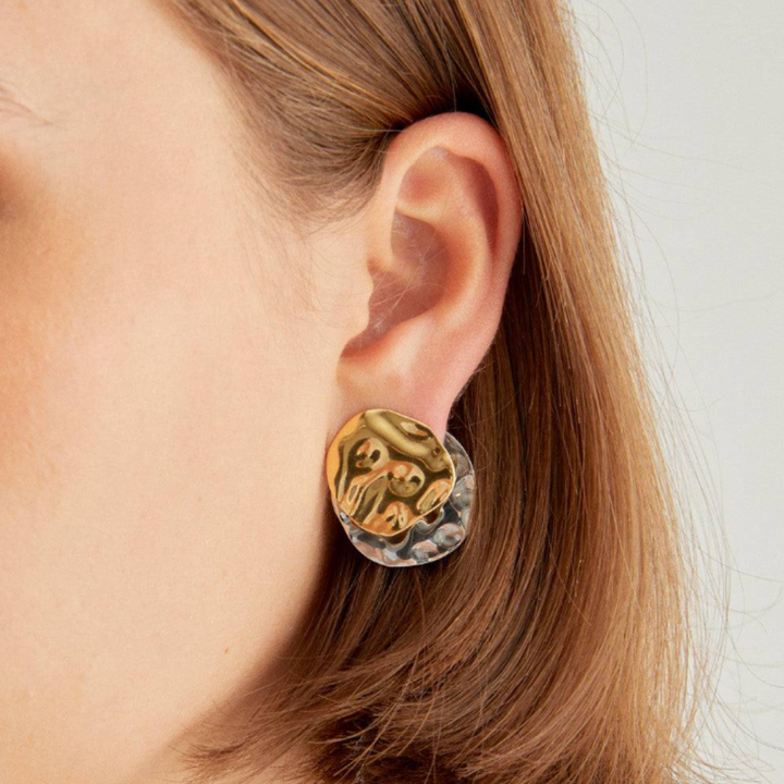 Gold and silver earring worn by a person with light brown hair.