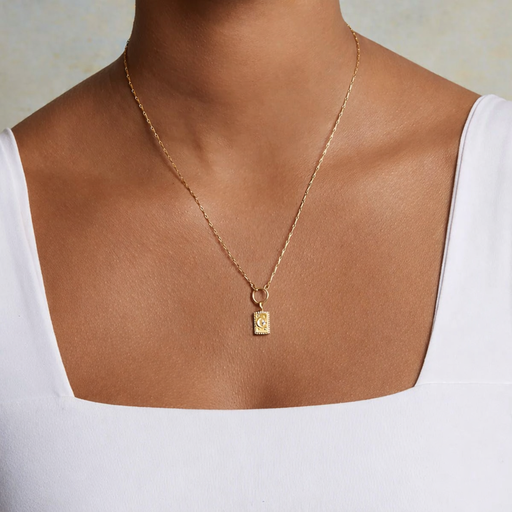 Gold necklace with a pendant on a person wearing a white top against a neutral background