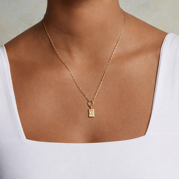 Gold necklace with a pendant on a person wearing a white top against a neutral background