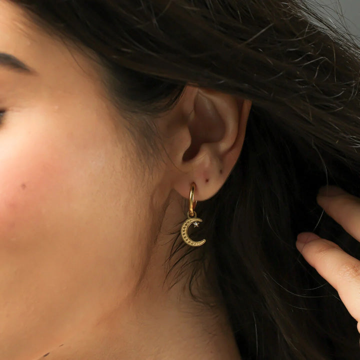 Close-up of a person wearing a gold earring with a moon design.