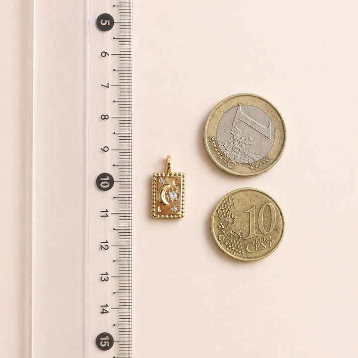 Small gold pendant and two coins next to a ruler on a light pink background