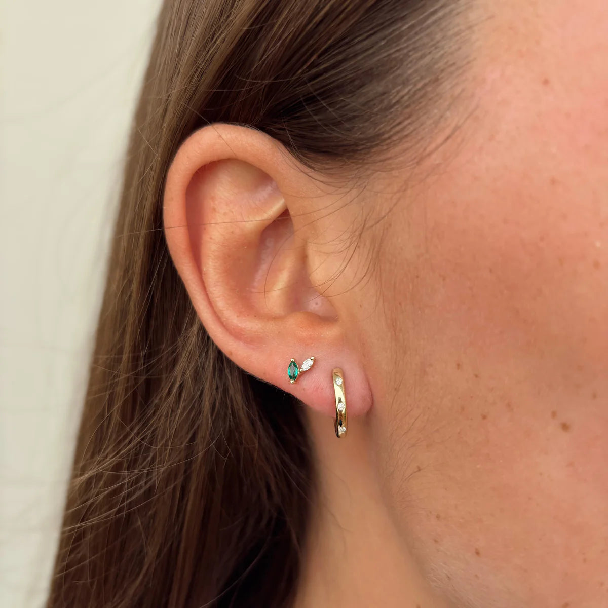 Close-up of an ear wearing a small earring and gold hoop.
