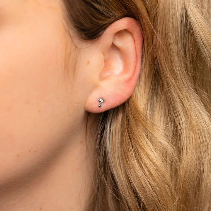 Close-up of an ear with a small earring worn by a person with blonde hair.