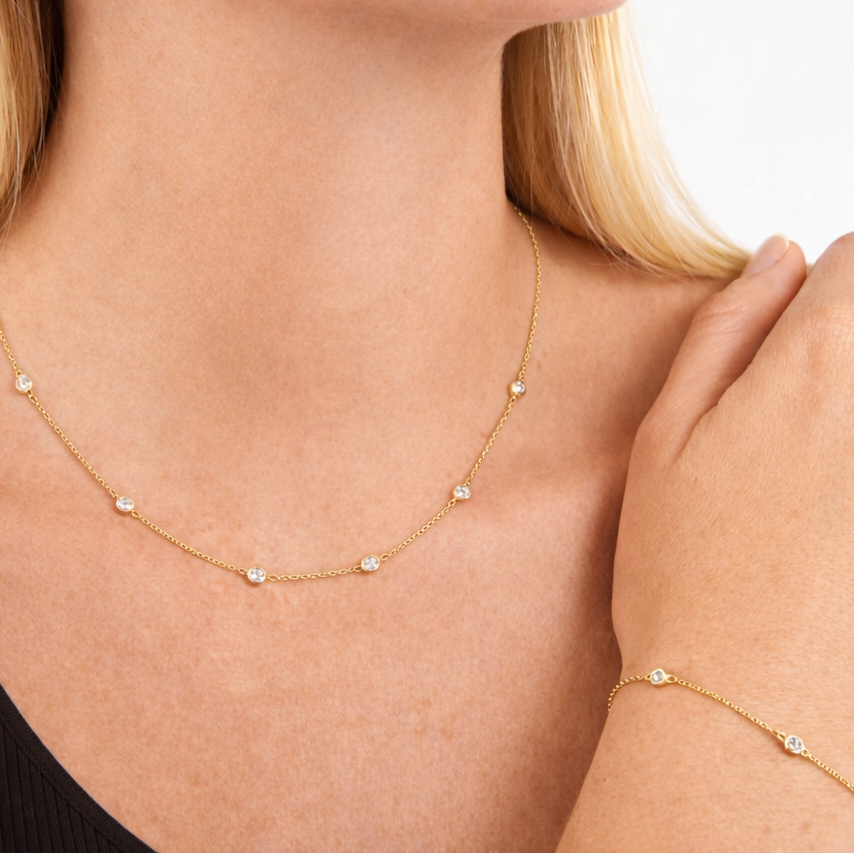 Gold necklace and bracelet on a person with a neutral background