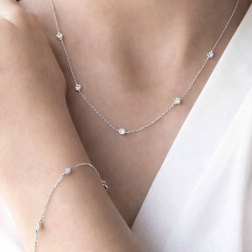 Silver necklace with small diamonds on a person wearing a white top.