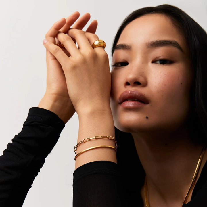 Woman wearing gold jewelry including rings and bracelets on a plain background