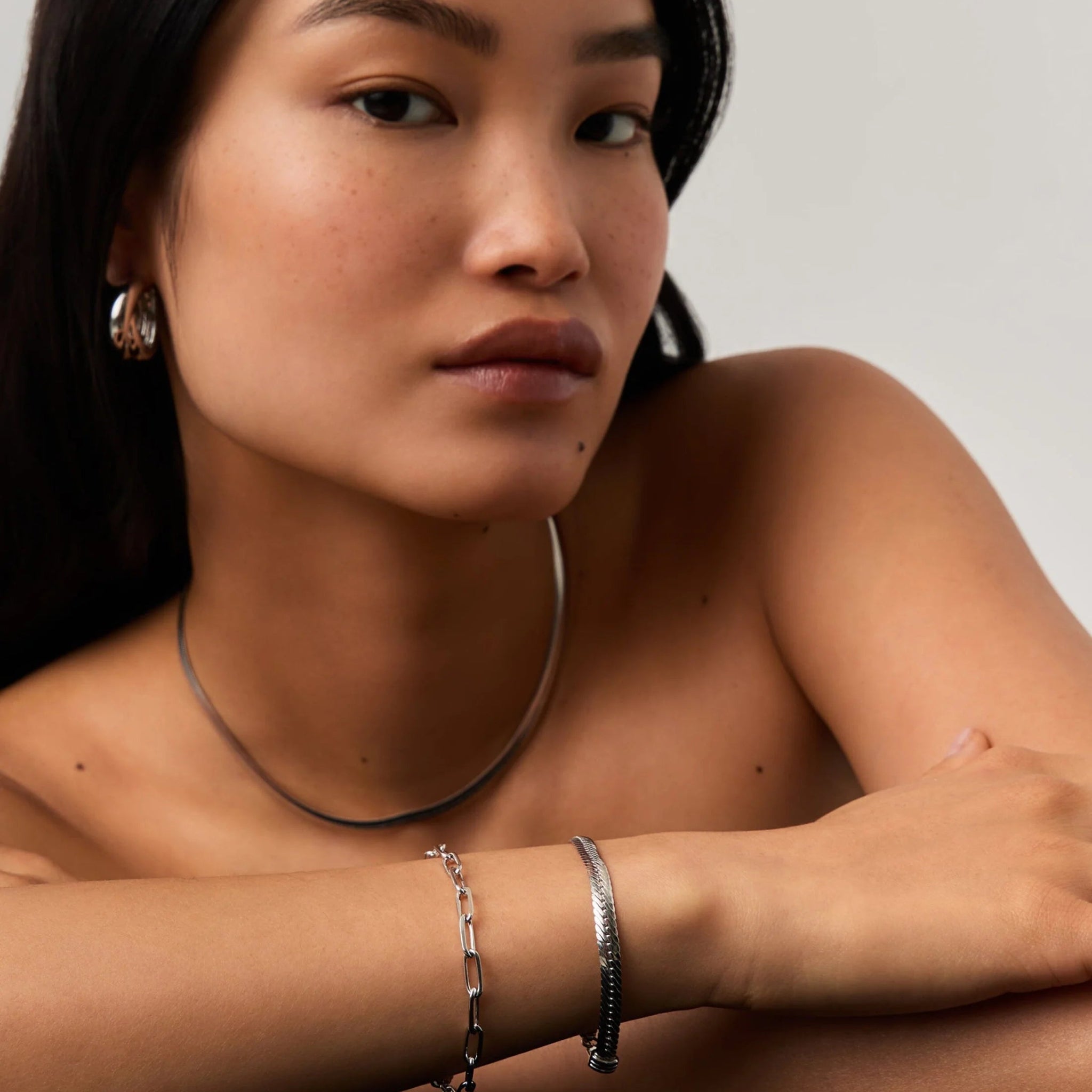 Woman wearing silver jewelry including earrings, necklace, and bracelets on a neutral background