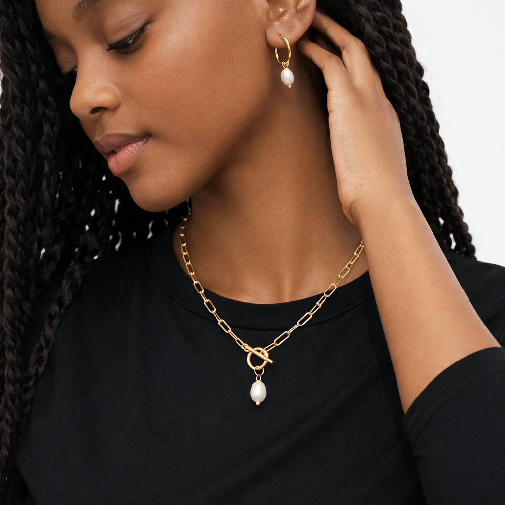 Woman wearing gold chain necklace and earrings with pearl drops.