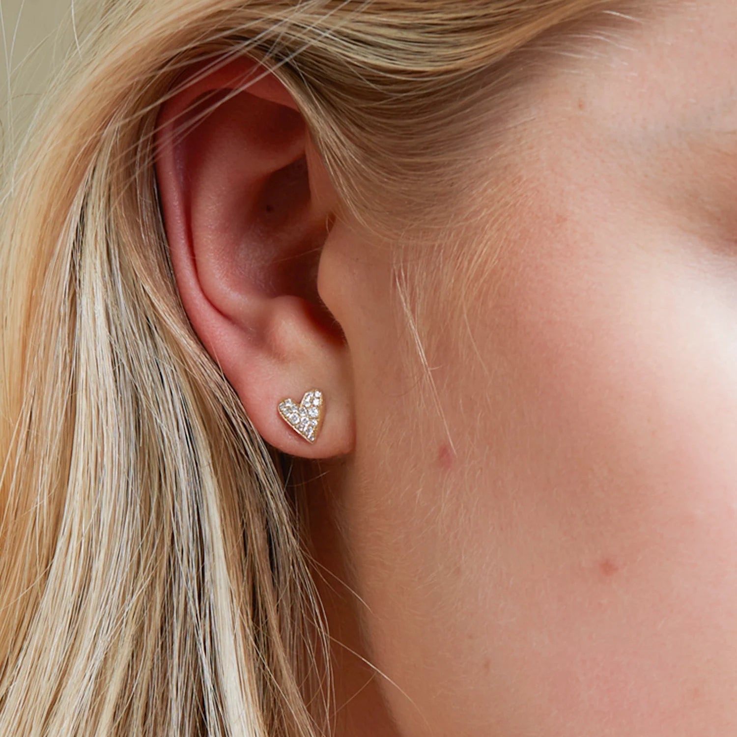 Close-up of an ear wearing a heart-shaped earring with blonde hair.