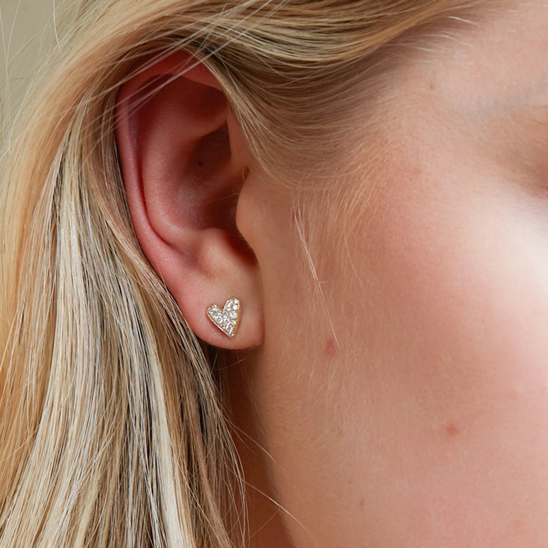 Close-up of an ear wearing a heart-shaped earring with blonde hair.