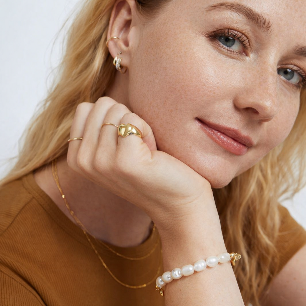 Woman wearing gold earrings, ring, and pearl bracelet against a white background