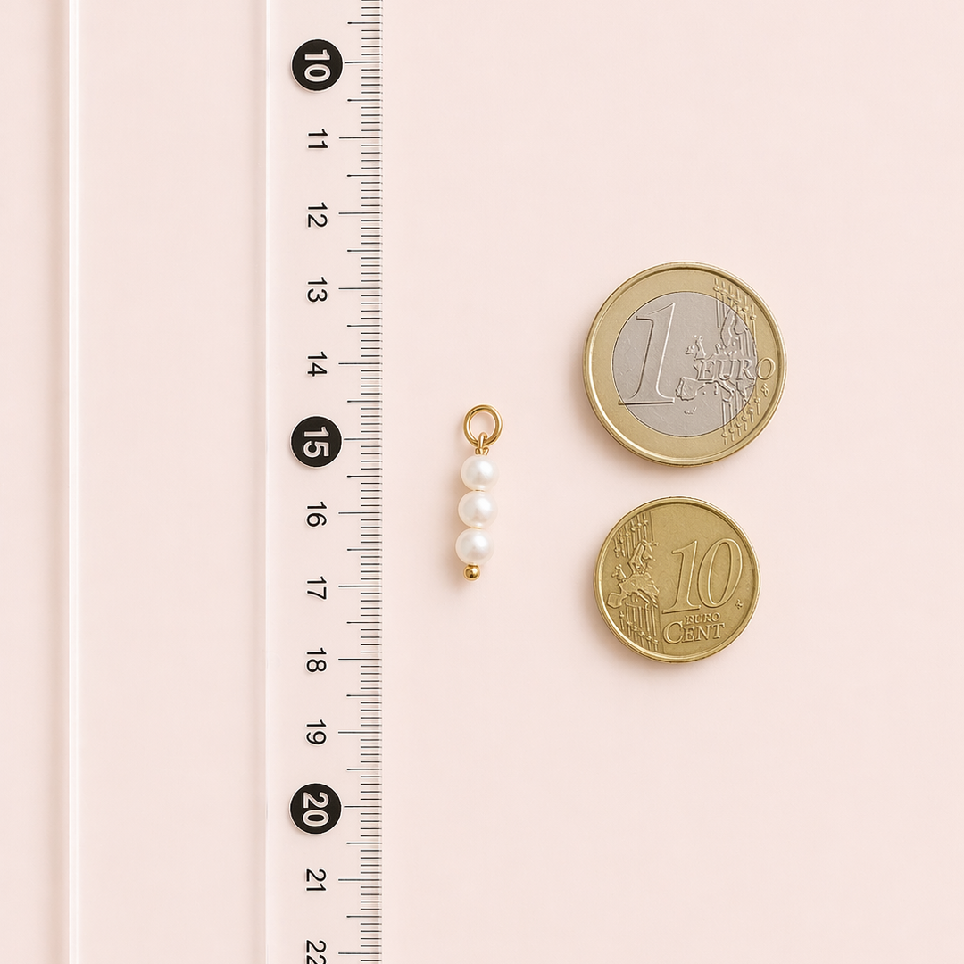 Two gold coins and a gold necklace with pearls next to a ruler on a pink background