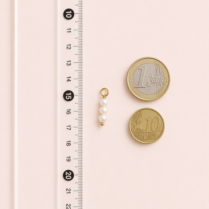 Two gold coins and a gold necklace with pearls next to a ruler on a pink background