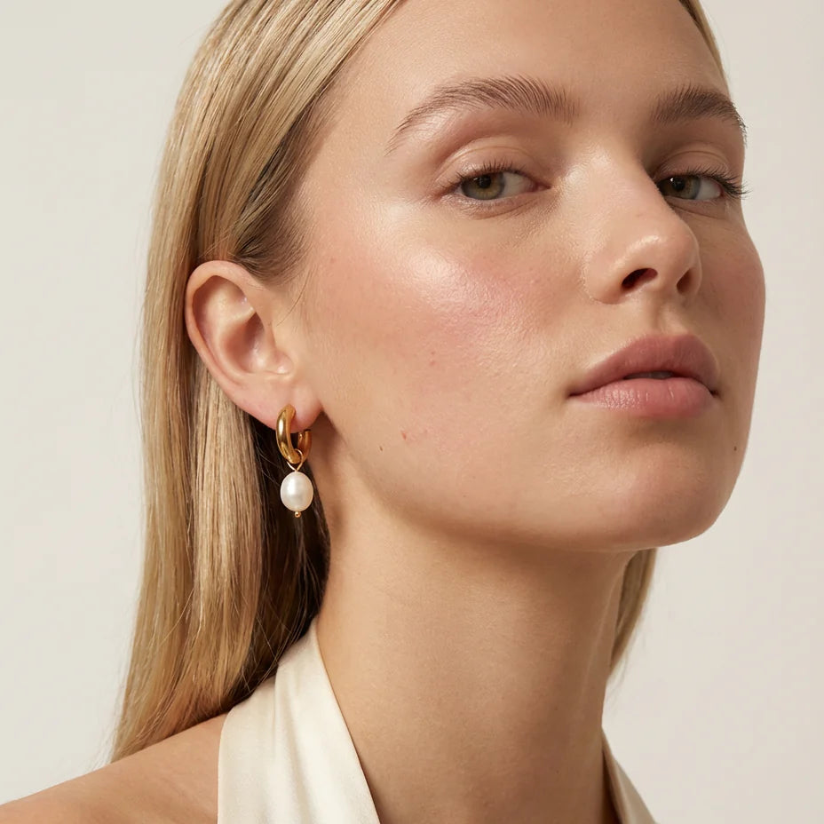 Close-up of a woman wearing pearl earrings with a neutral background