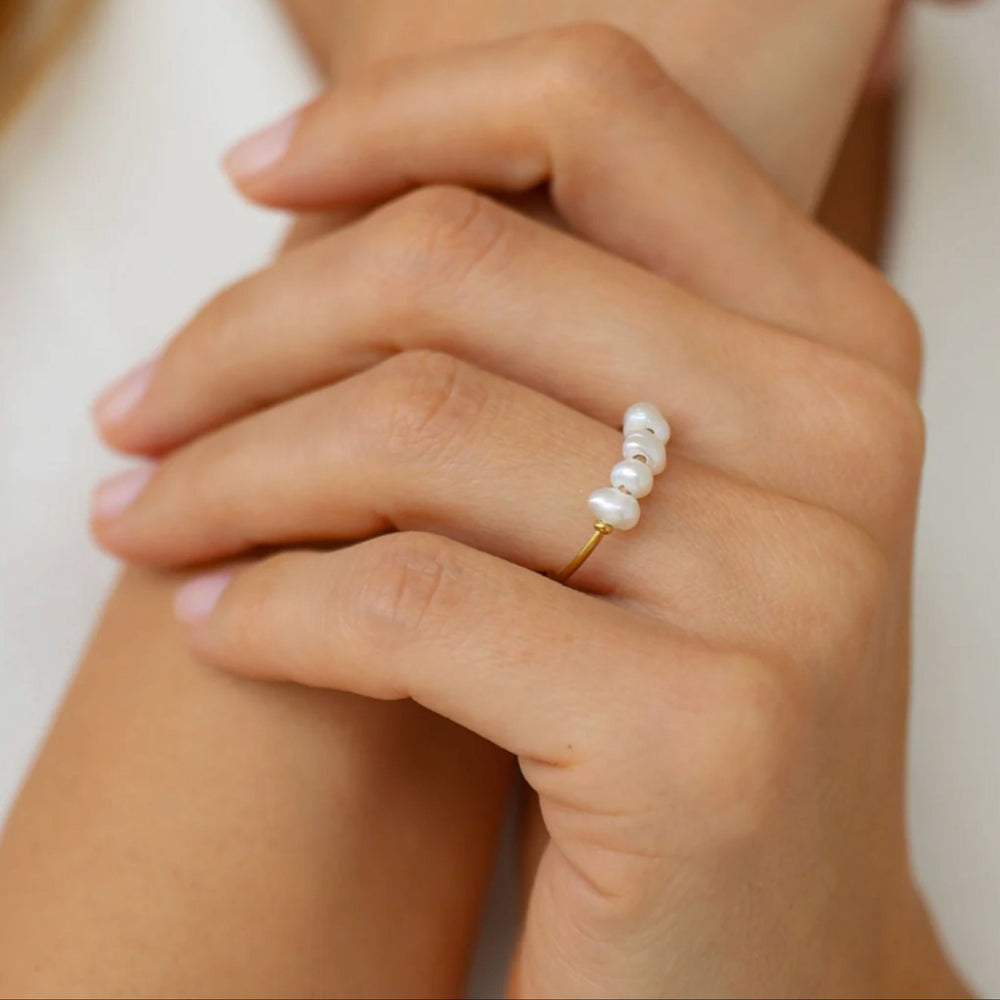 Hand wearing a gold ring with pearls on a neutral background