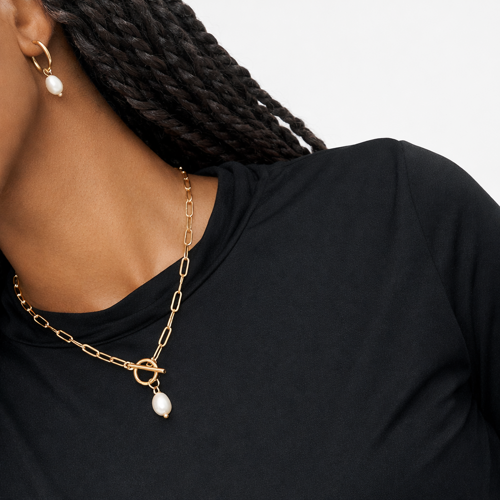 Gold chain necklace with pearl pendants worn by a person against a black background