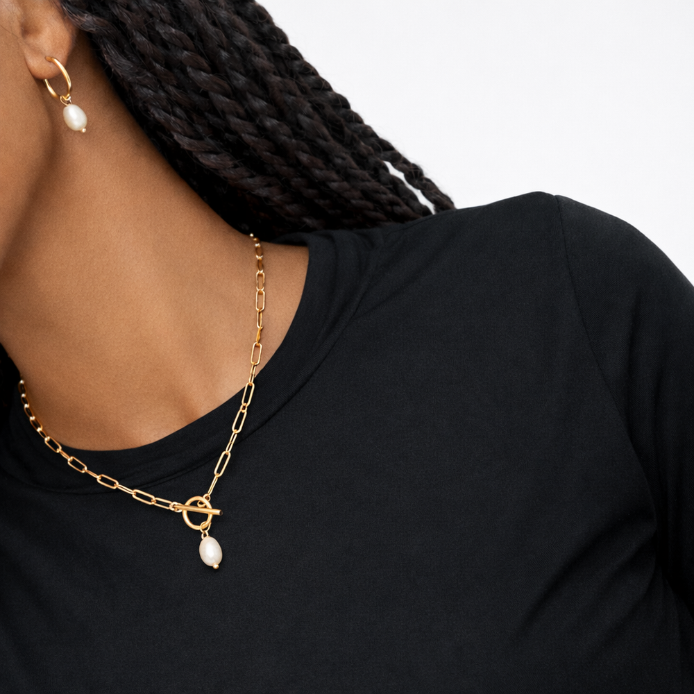 Gold chain necklace with pearl pendants worn by a person against a neutral background