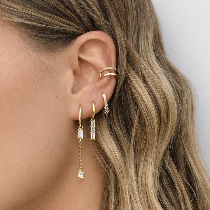 Close-up of an ear with gold earrings and a ring, against a neutral background