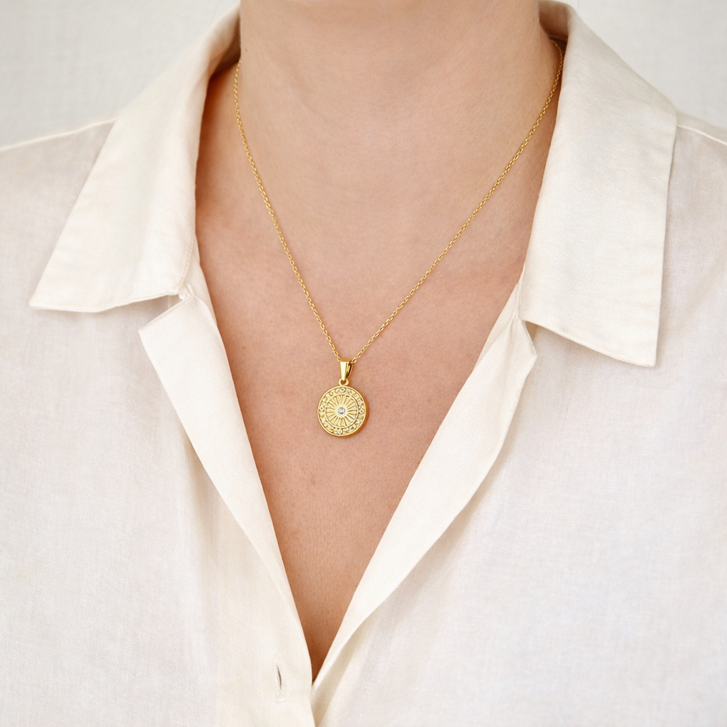 Gold necklace with a circular pendant worn by a person in a white shirt.
