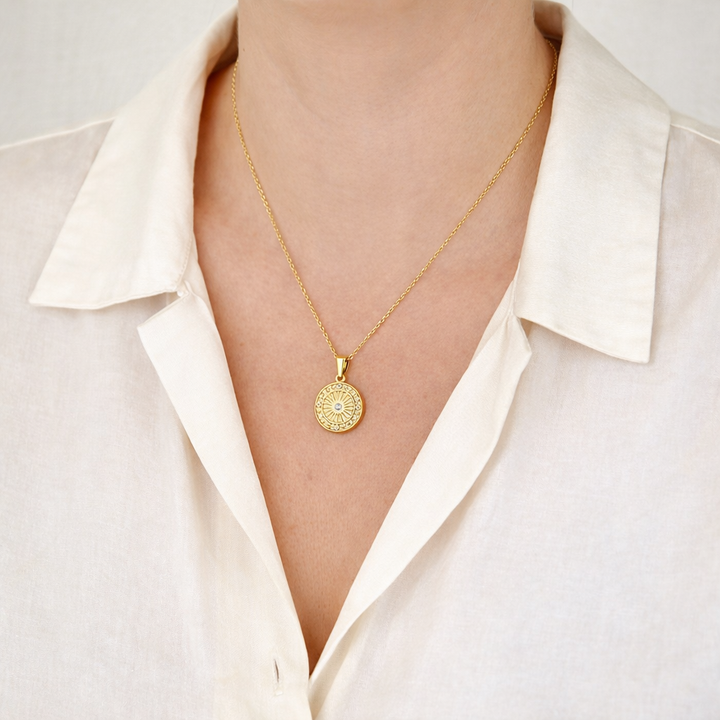 Gold necklace with a circular pendant worn by a person in a white shirt.