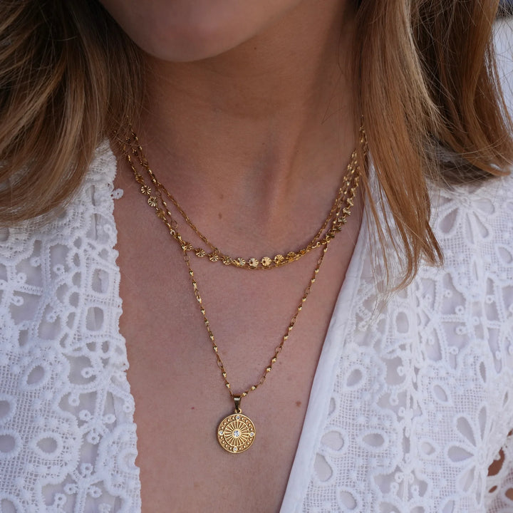 Close-up of a person wearing two gold necklaces with a white lace top.