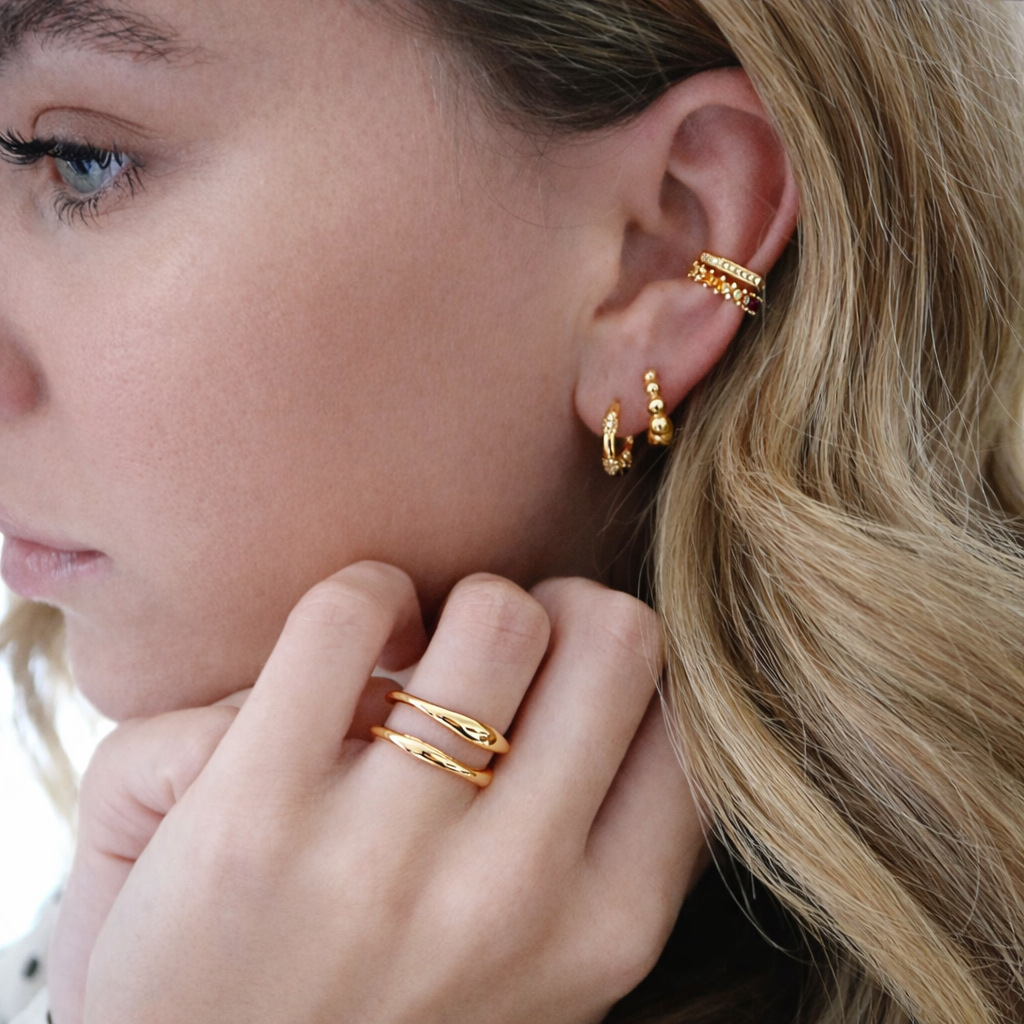 Close-up of a person wearing gold earrings and rings with a blurred background