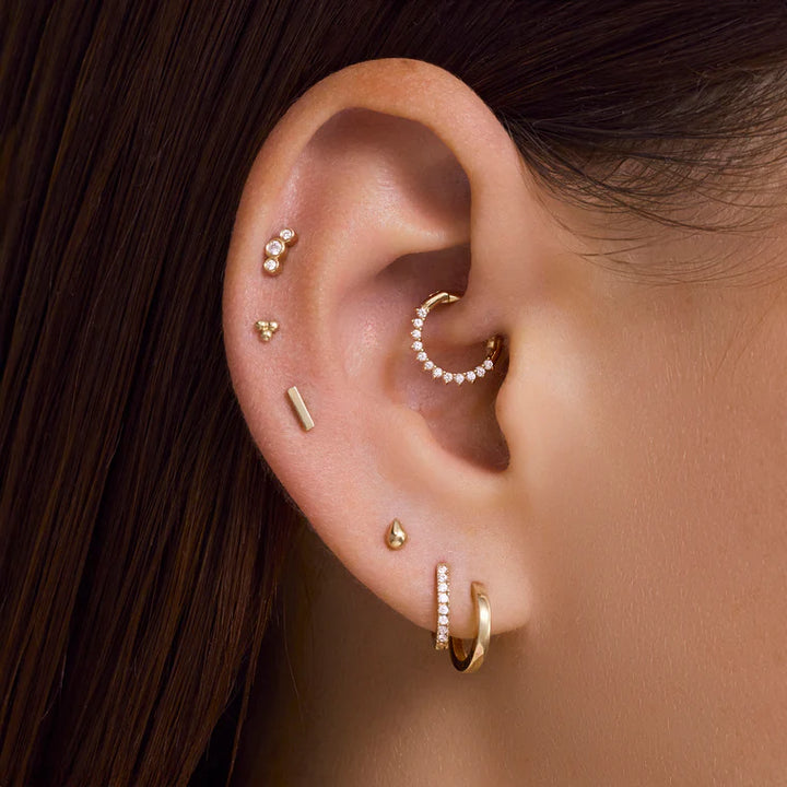Close-up of an ear with multiple gold earrings on a blurred background