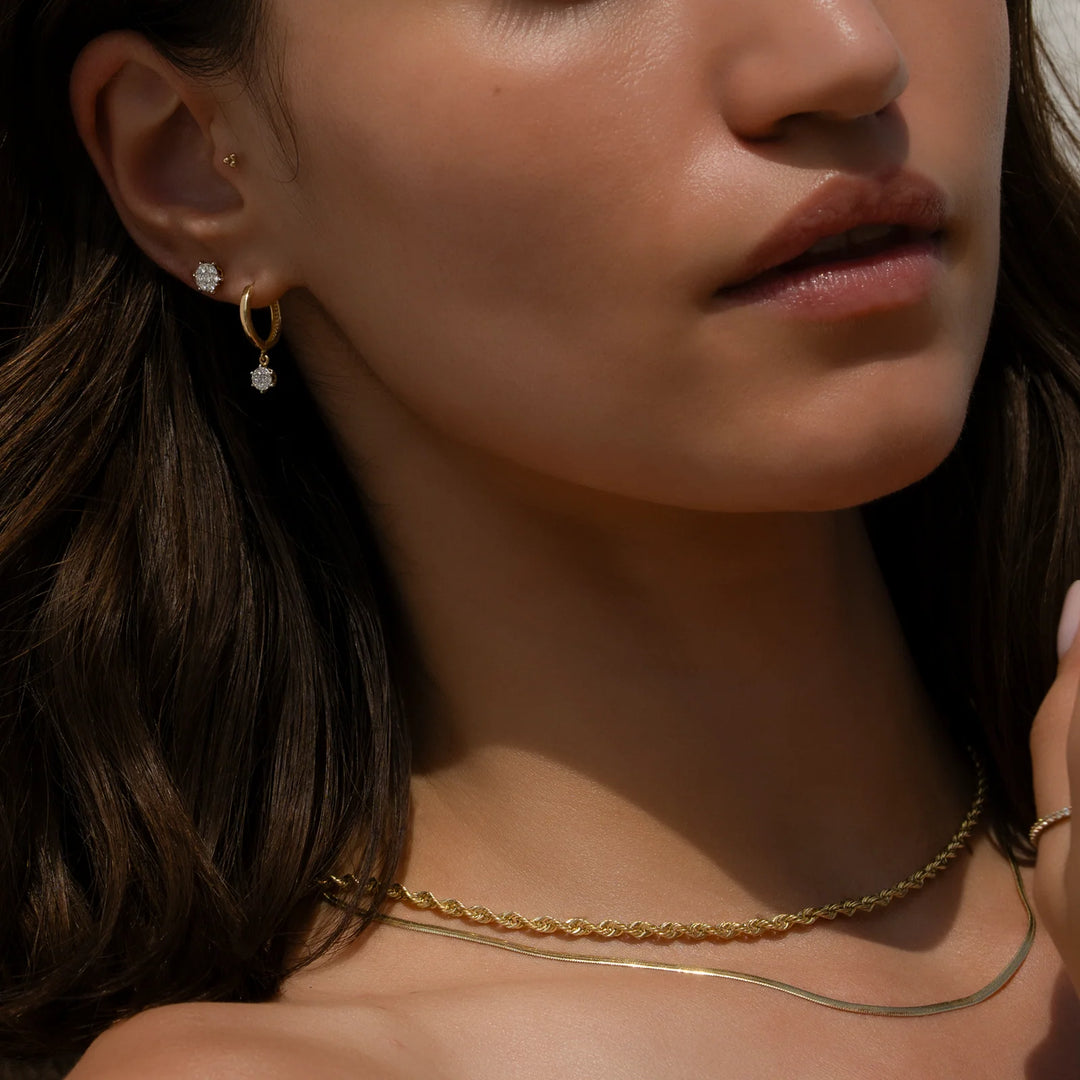 Close-up of a woman wearing gold earrings and a necklace with a warm, soft focus.