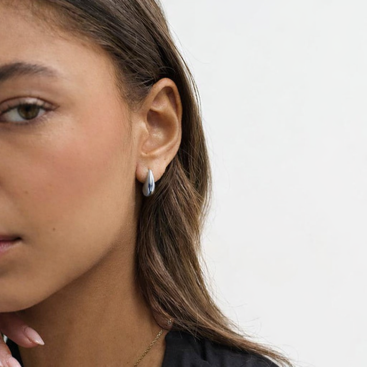Close-up of a person wearing a small hoop earring on a plain background