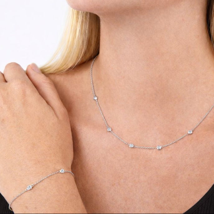 Silver necklace and bracelet on a person's wrist with a plain background
