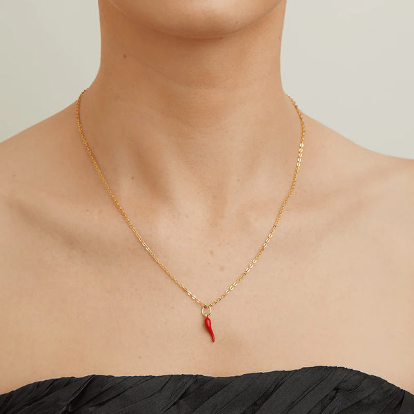 Gold necklace with a red pendant on a person wearing a black top against a neutral background