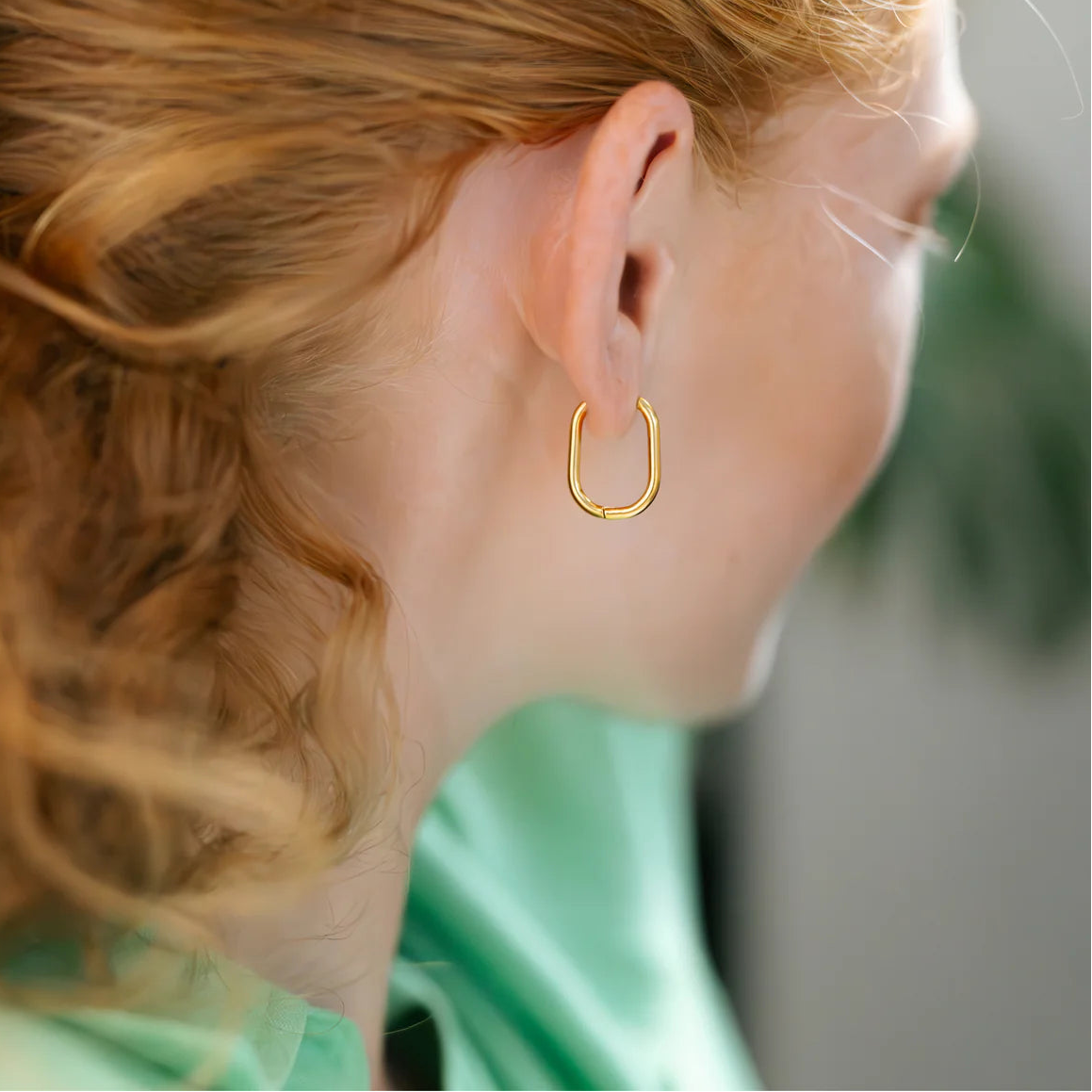 Close-up of a person wearing a gold hoop earring with a blurred background