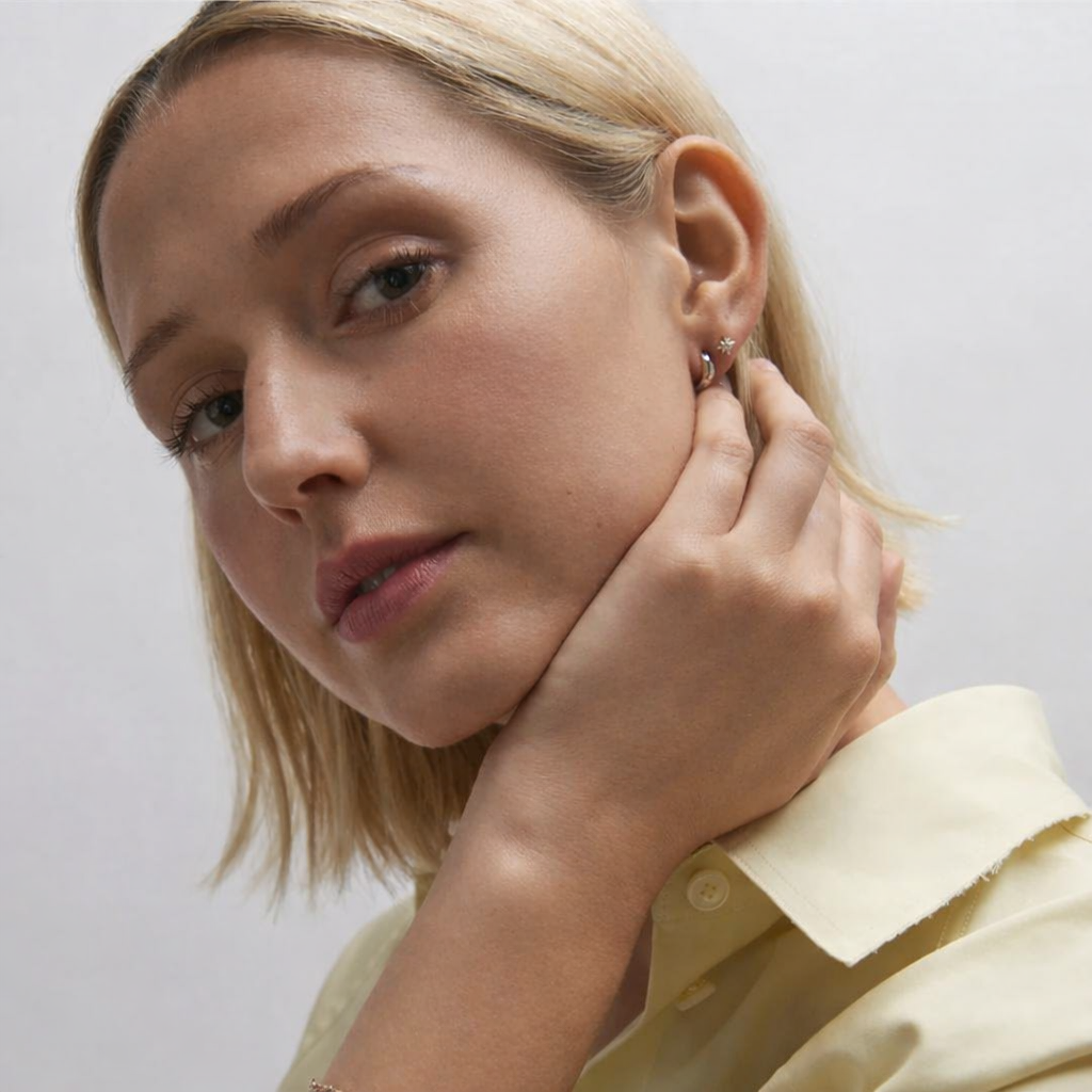 Woman adjusting an earring against a plain background