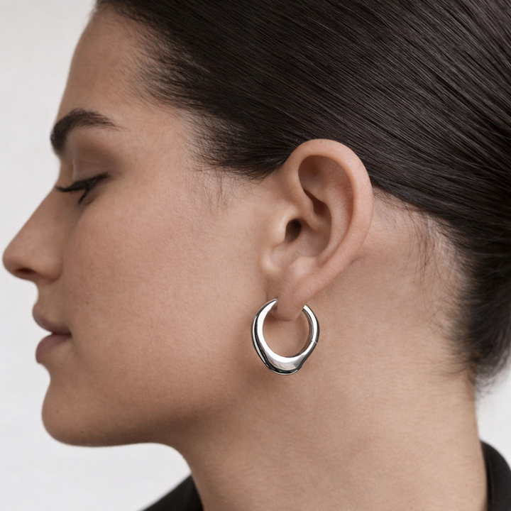 Close-up of a woman wearing a silver hoop earring on a plain background
