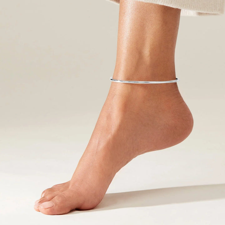 Close-up of a foot wearing a silver anklet on a neutral background