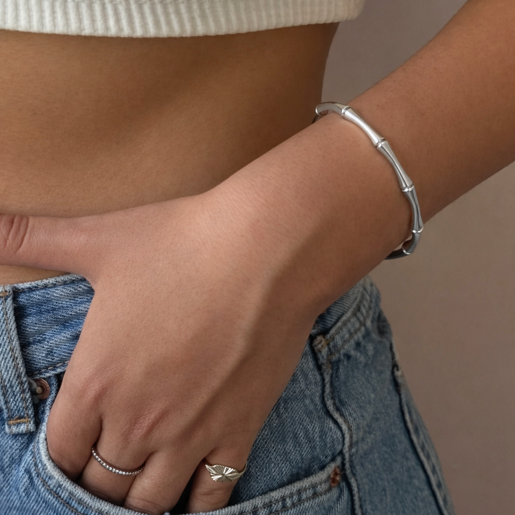 Person wearing a silver bracelet and ring on a neutral background