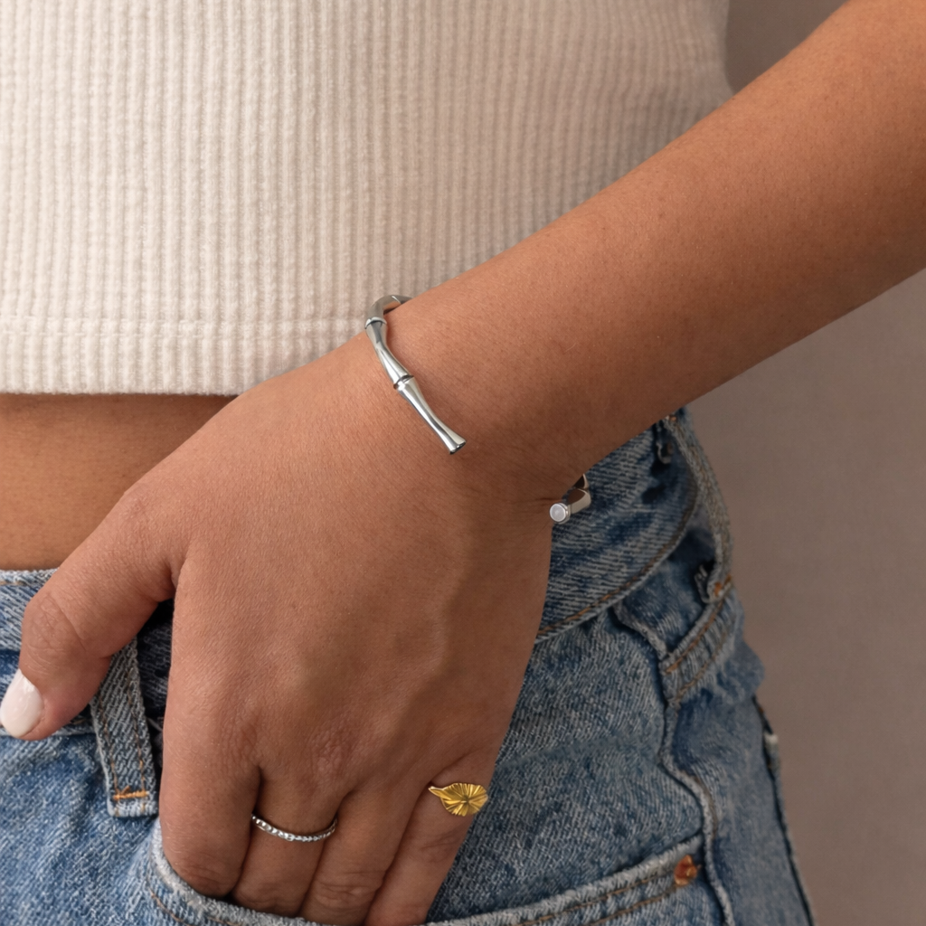 Person wearing a gold ring and silver bracelet on a neutral background