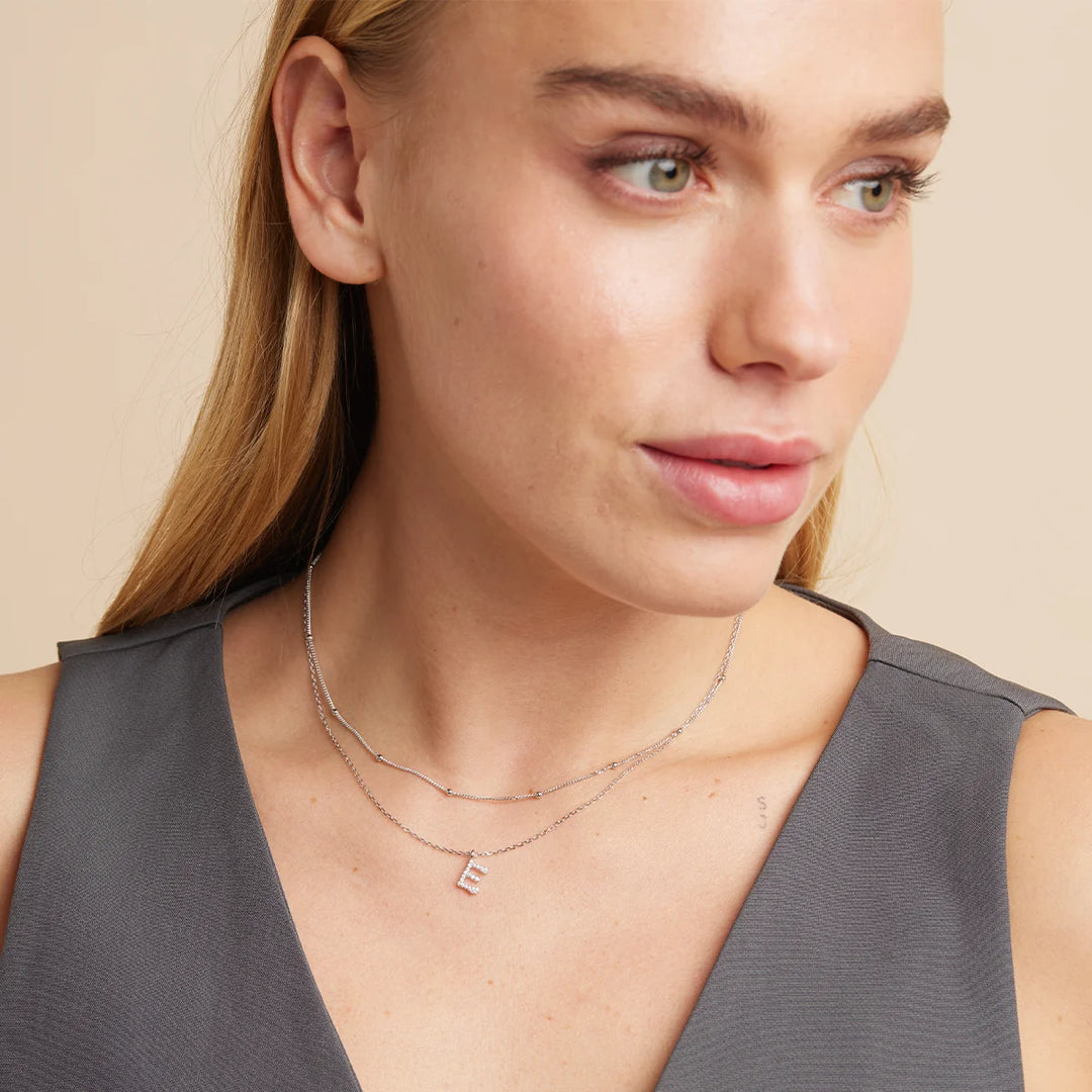 Woman wearing a delicate necklace with a small pendant on a beige background