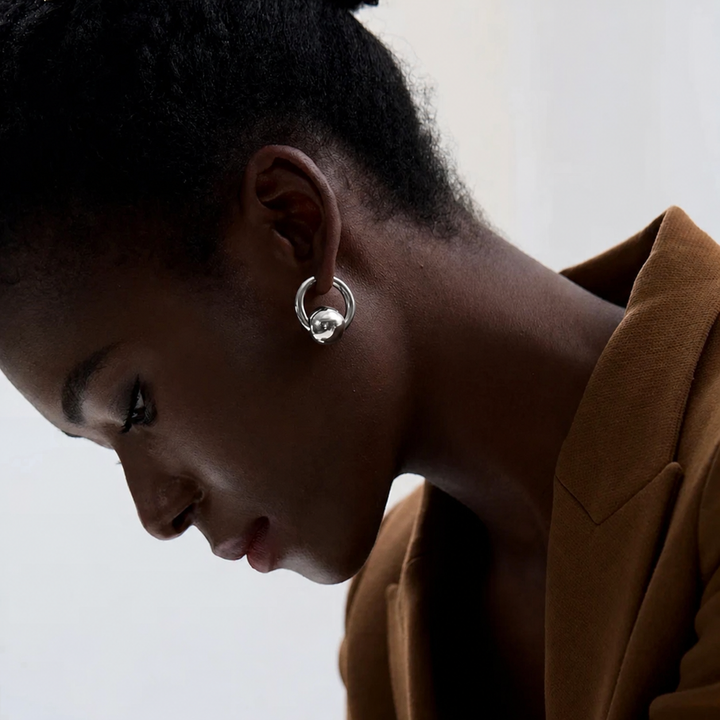 Close-up of a person wearing gold hoop earrings with a neutral background
