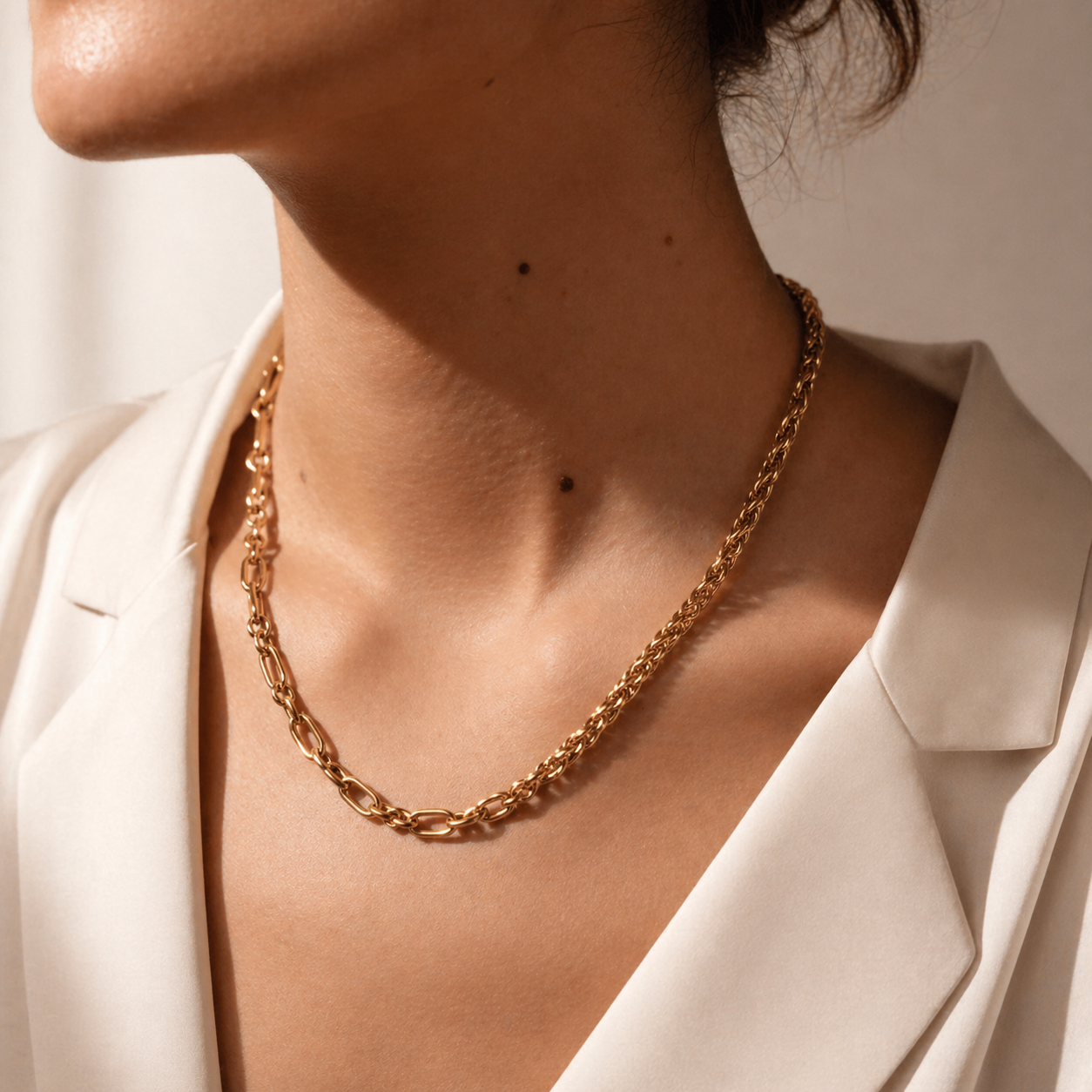 Gold chain necklace worn by a person in a white blazer.